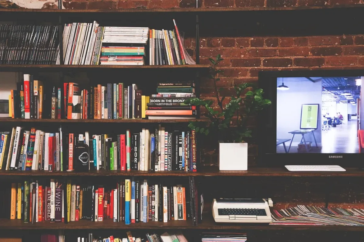 Telewizor umieszczony w salonie na tle regałów wypełnionych książkami, łączący strefę rozrywki z domową biblioteką.